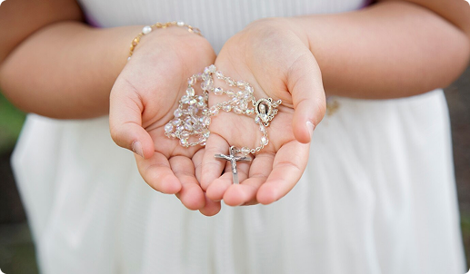 Child holding a rosary in their hands with a blurred background