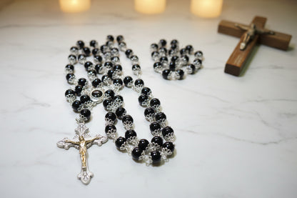 Black rosary with silver cross on a wooden surface